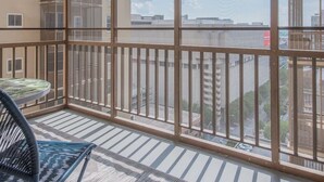 Un balcone con ringhiera in vetro, un tavolo rotondo e una sedia in vimini.