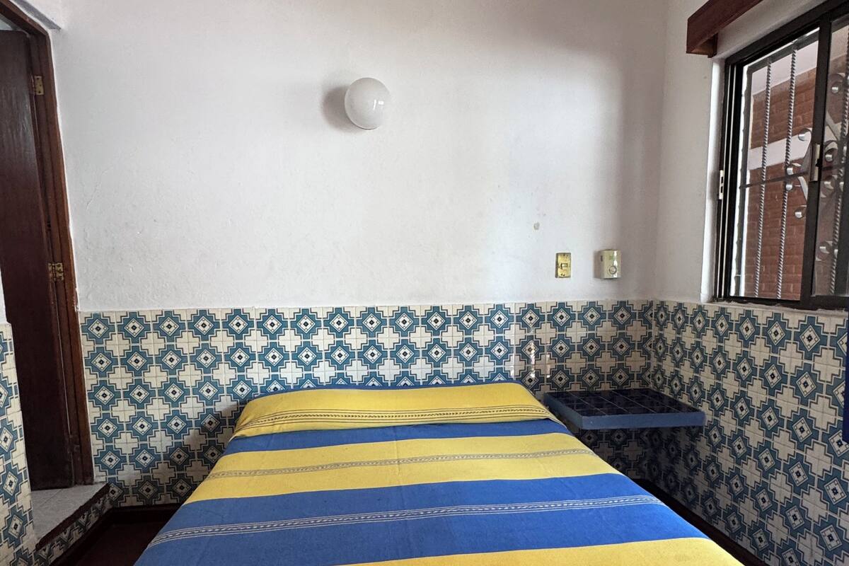 A room with a bed, a ceiling fan, patterned walls, and a window with bars.