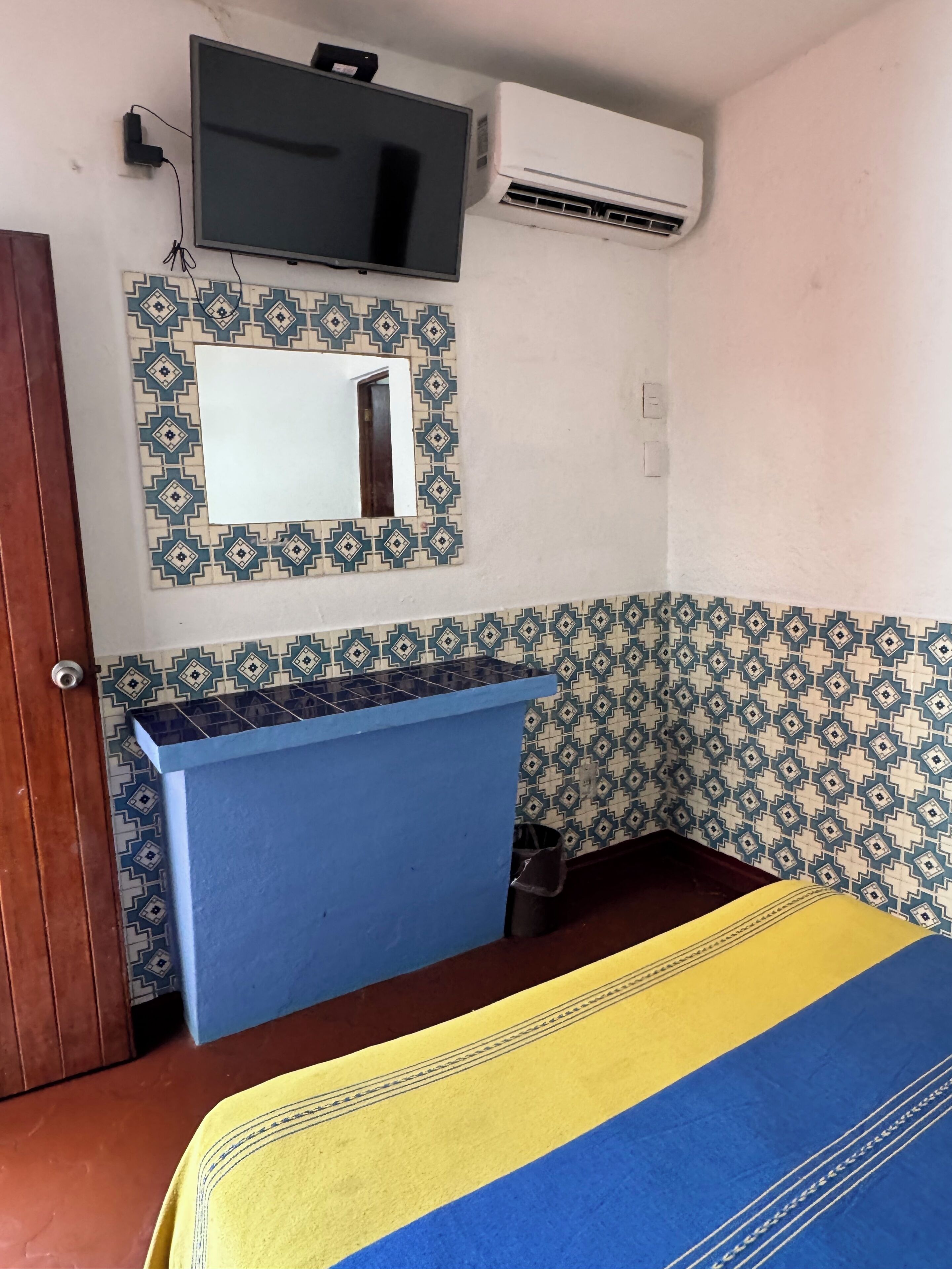 A room with a bed, a blue bedside table, a mirror, an air conditioner, and patterned walls.