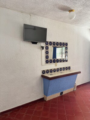 A room with a television mounted on the wall, a mirror with decorative tiles, and a blue countertop. - Hotel California (Mazatlán)