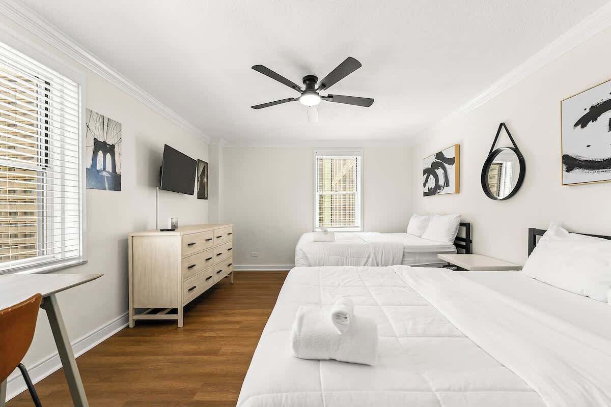 A bedroom with two beds, a ceiling fan, a dresser, and artwork on the walls.