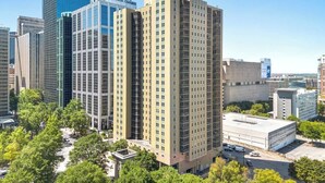Un edificio alto con fachada de vidrio moderna, rodeado de otros edificios elevados y áreas verdes.