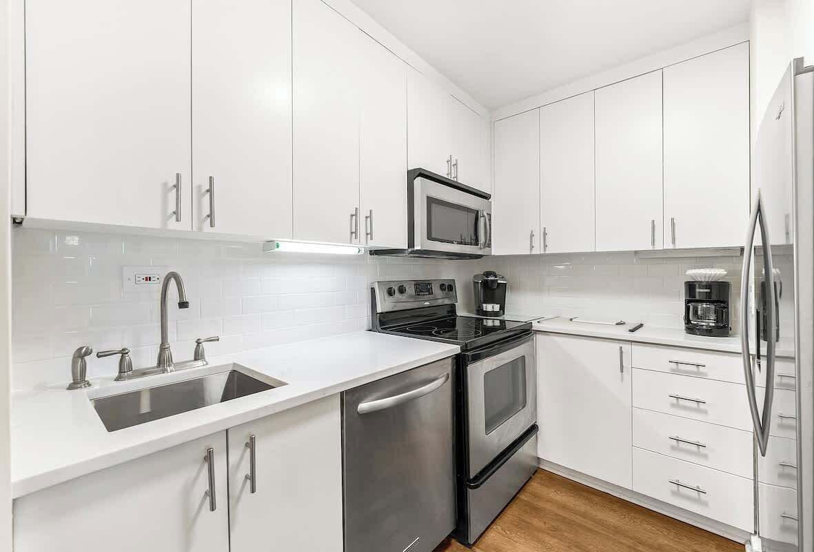 Una cucina moderna con mobili bianchi, elettrodomestici in acciaio inossidabile, un lavello doppio e un forno integrato.