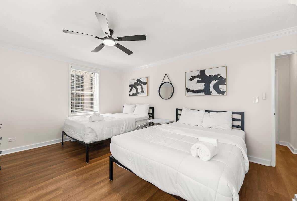 A hotel room with two beds, a ceiling fan, and abstract artwork on the walls.