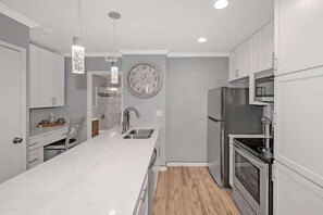A modern kitchen with white cabinetry, stainless steel appliances, and a large island with a sink. - Central 1BR w/ Walkable Hotspots (Atlanta)