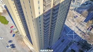 Un edificio alto con diversi piani, un parcheggio con parecchie auto e una strada con un attraversamento pedonale.