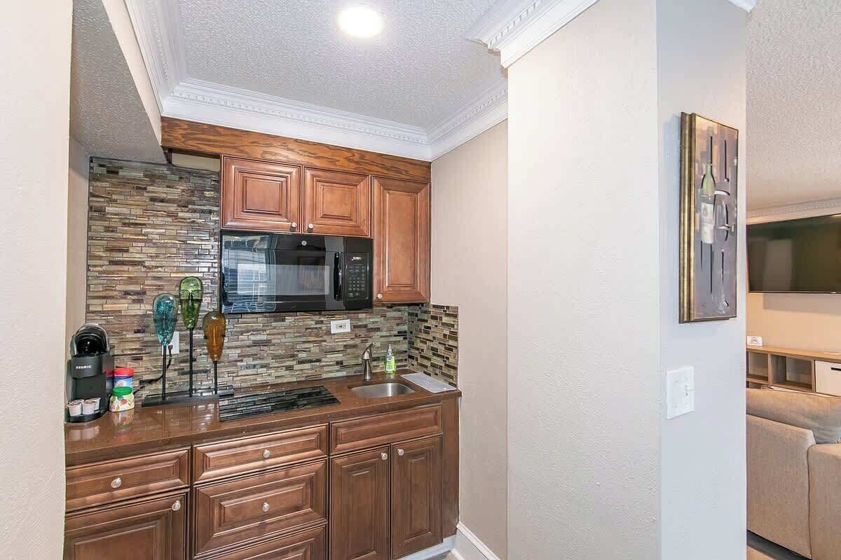 A compact kitchen with wooden cabinets, a microwave, and a backsplash with mosaic tiles.