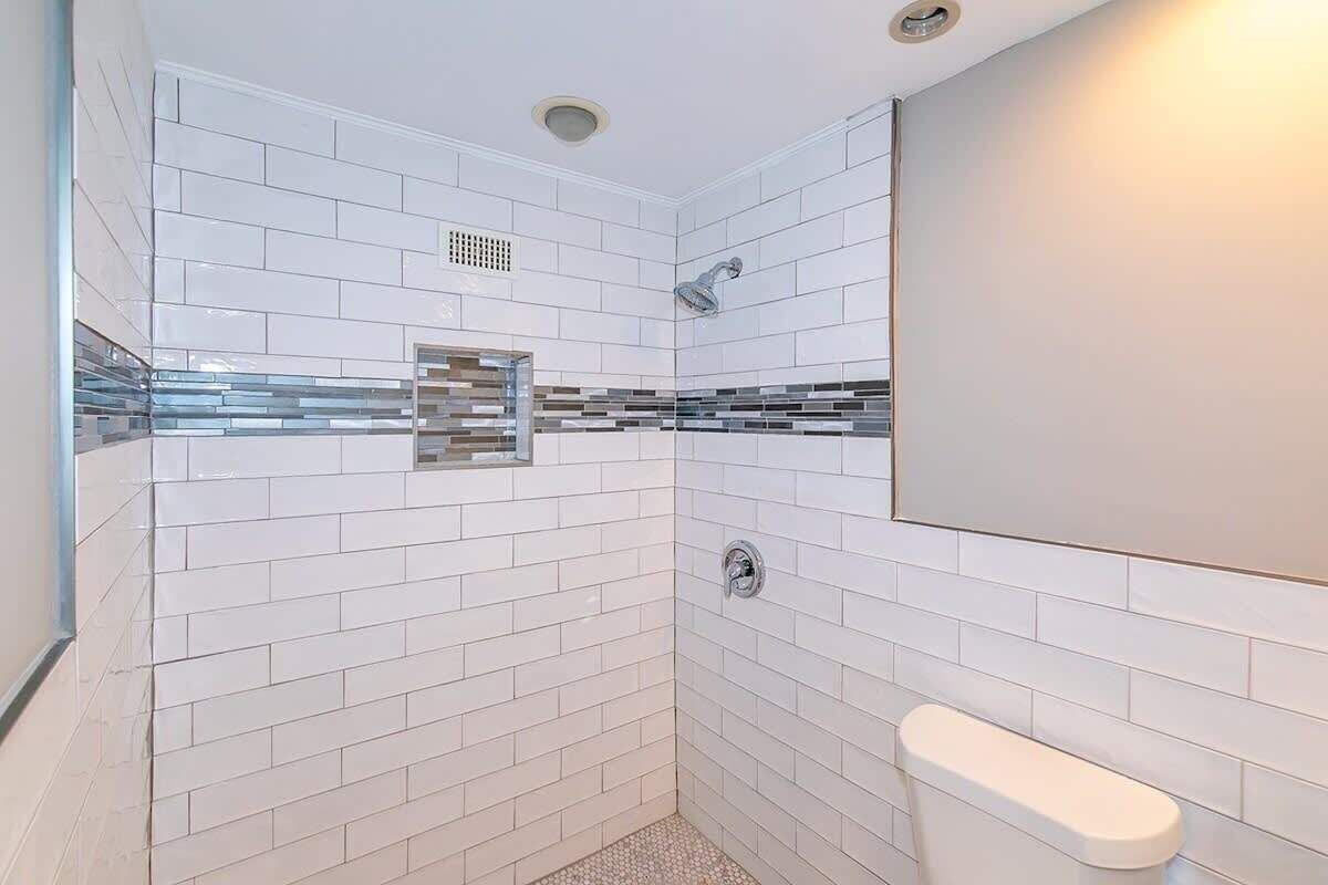 Un baño moderno con azulejos blancos tipo metro, cabina de ducha de vidrio y un inodoro blanco.