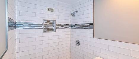 Un baño moderno con azulejos blancos tipo metro, cabina de ducha de vidrio y un inodoro blanco.