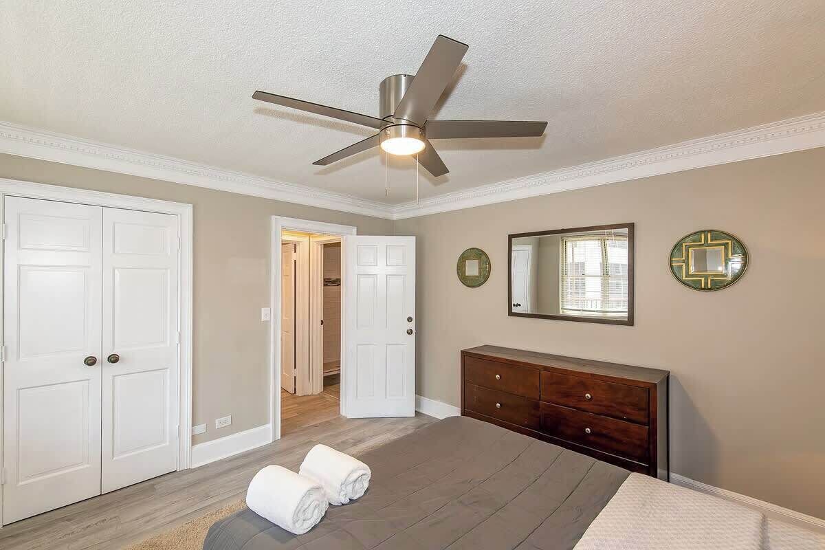 A bedroom with a bed, a dresser, a ceiling fan, and a door leading to a bathroom.