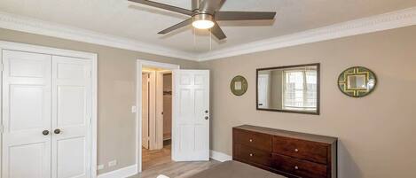 A bedroom with a bed, a dresser, a ceiling fan, and a door leading to a bathroom.