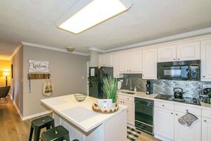 Une cuisine moderne avec des meubles blancs, un réfrigérateur noir, une cuisinière en acier inoxydable et un dosseret carrelé.