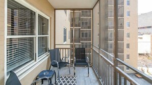 Ein Balkon mit zwei Stühlen und einem kleinen Tisch, mit Blick auf ein Gebäude mit zahlreichen Fenstern und Balkonen.