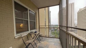 A balcony with a table and chairs, a window, and a view of tall buildings. - Bright Downtown Retreat w/ Full Kitchen (Atlanta)