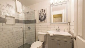 A bathroom with a glass shower enclosure, a toilet, a sink with a mirror above, and a wall-mounted towel rack. - Bright Downtown Retreat w/ Full Kitchen (Atlanta)