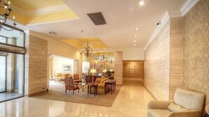 A spacious lobby with a polished floor, a seating area with sofas and chairs, and a chandelier. - Cozy High-Rise Condo Near AmericasMart (Atlanta)