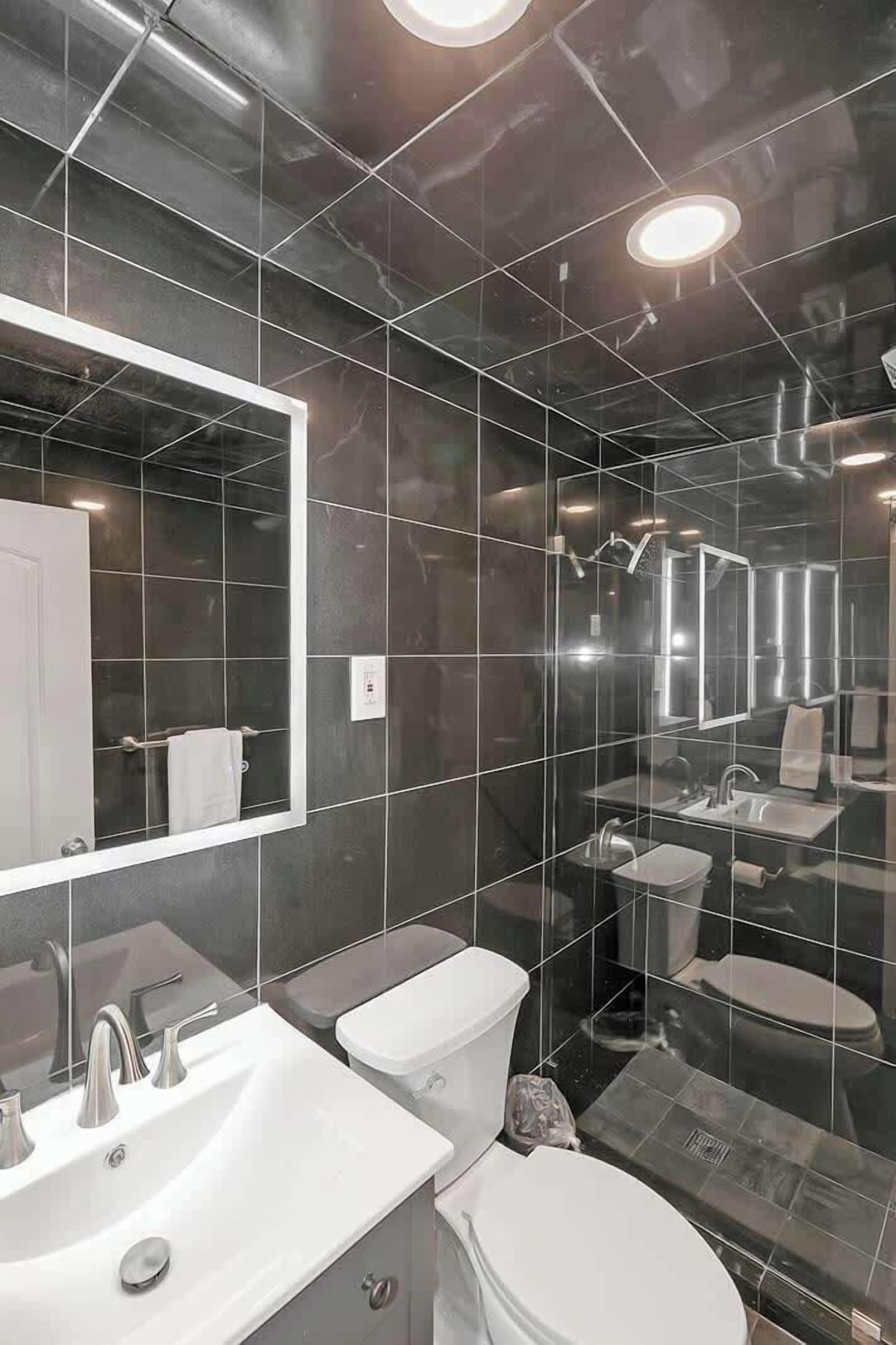 A modern bathroom with dark tiled walls, a large mirror, and two sinks.