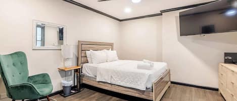 A modern bedroom with a bed, a green chair, a TV, and a ceiling fan.