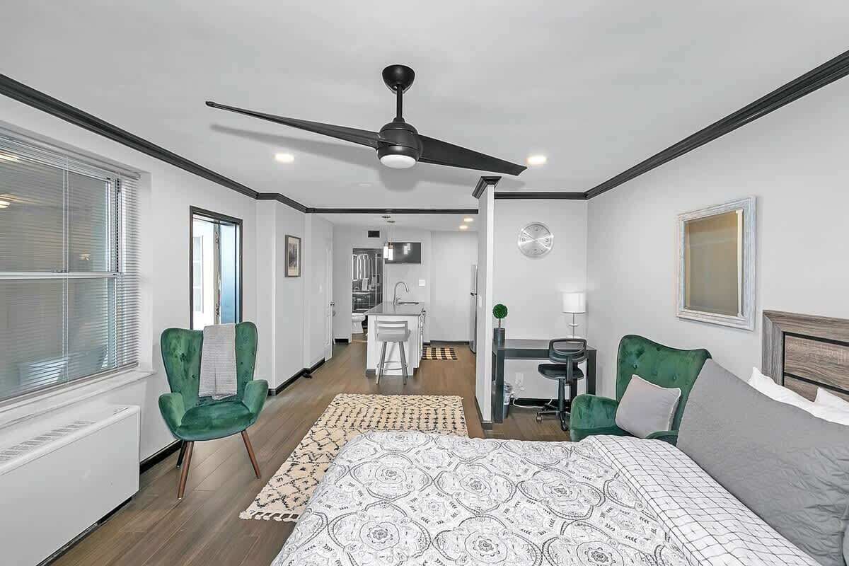 A modern hotel room with a large bed, a ceiling fan, a desk with a chair, and a view of the hallway.