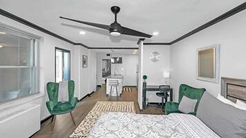 A modern hotel room with a large bed, a ceiling fan, a desk with a chair, and a view of the hallway.