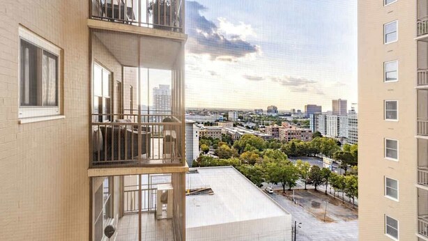 Een meerlaags gebouw met balkons, grote ramen en uitzicht op een stadsgezicht met bomen en gebouwen.