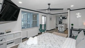 Een moderne slaapkamer met een groot bed, een plafondventilator, een bureau en uitzicht op de stad door het raam.