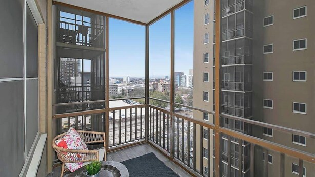 Ein Balkon mit Blick auf eine Stadtansicht, ein Korbstuhl und ein kleiner Tisch mit einer Pflanze.