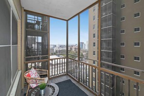 A balcony with a view of a cityscape, a wicker chair, and a small table with a plant. - ATL Hotel District Condo w/Balcony (Atlanta)
