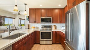 A modern kitchen with wooden cabinets, stainless steel appliances, a double sink, and pendant lighting. - VERY SPECIAL  Renovated 1 Bdrm Condo - A/C - Oceanview, Athletic Club Access (Koloa)
