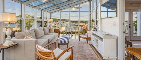 A conservatory with a sofa, chairs, a table, and a view of a marina.