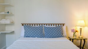 Ein ordentlich bezogenes Bett mit einer Bettdecke in Weiß und Blau, zwei passende Kissen sowie ein Nachttisch mit Lampe und Blumenvase.