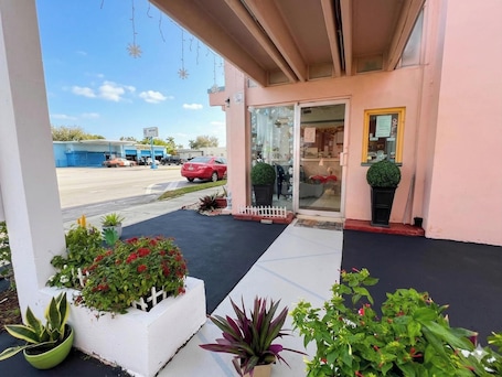 A building entrance with a glass door, potted plants, and a clear view of a parking lot with cars.