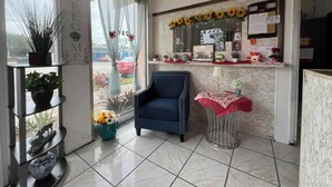 A reception area with a blue armchair, a small table with a red tablecloth, and a shelf with plants. - Anhinga Motel Homestead Fl (Homestead)