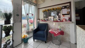 A reception area with a chair, a small table with a red tablecloth, and a window with a 'WELCOME' sign. - Anhinga Motel Homestead Fl (Homestead)