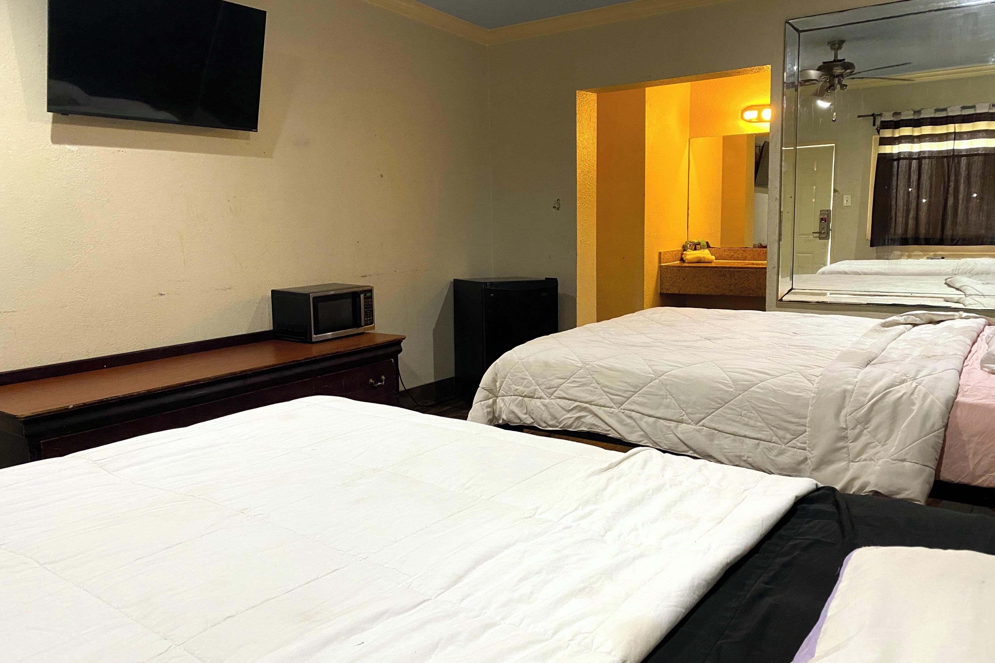 A hotel room with two beds, a television, a microwave, and a small cabinet.