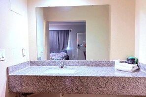 A bathroom with a granite countertop, a mirror, a sink, and a towel rack. - Regency Inn Houston Near Hobby Airport (Houston)