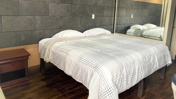 Ein Schlafzimmer mit einem Bett, dunklem Holzboden, einem Nachttisch und einem großen Spiegel.