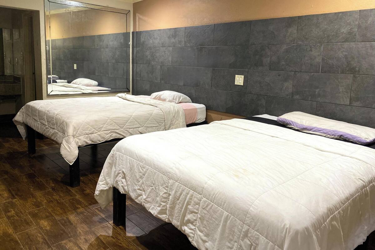 A hotel room with two beds, a large mirror, and a dark tiled wall.
