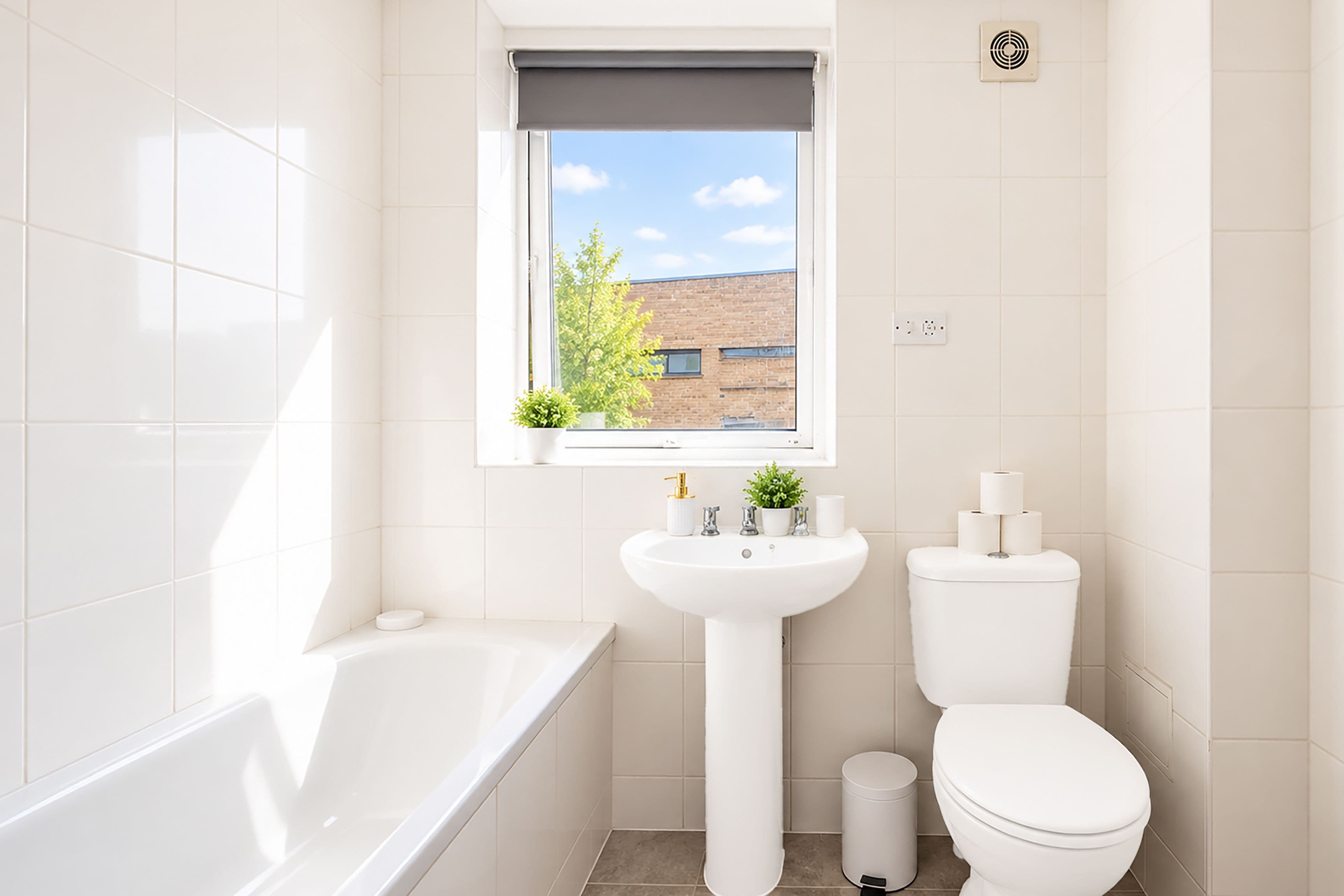 A bathroom with a bathtub, a sink, a toilet, and a window with a view of a building and trees.