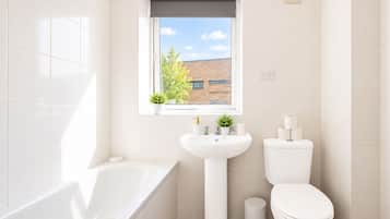 A bathroom with a bathtub, a sink, a toilet, and a window with a view of a building and trees.