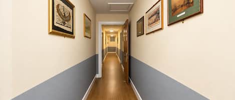 A hallway with framed artworks on the walls, a wooden floor, and a door at the end.
