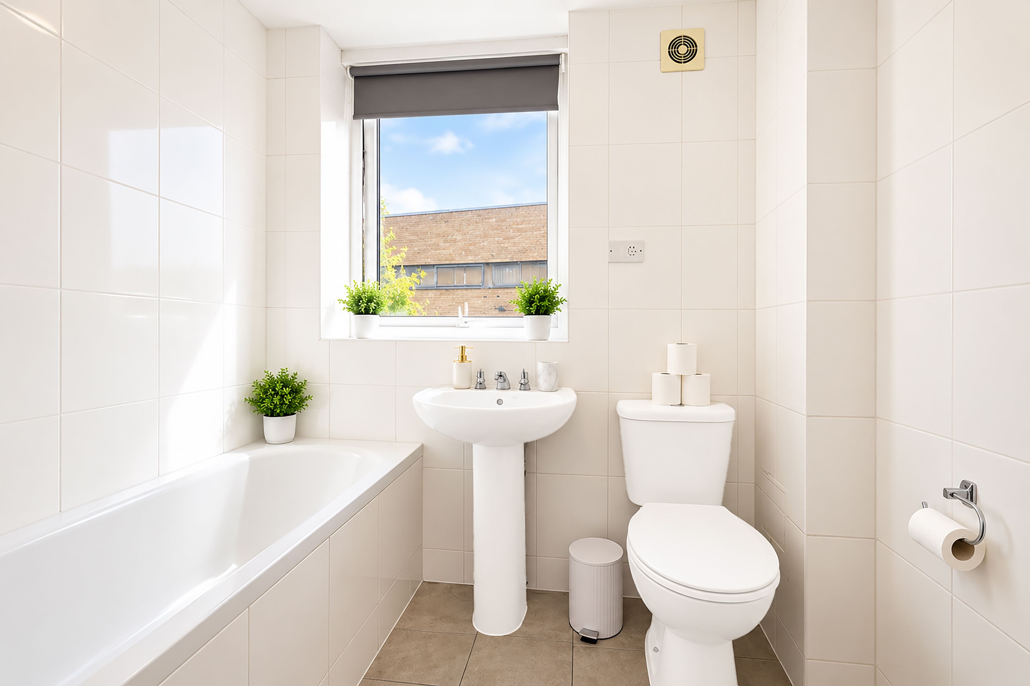 A modern bathroom with a bathtub, a sink, a toilet, and a window with plants.