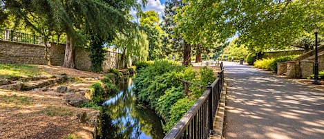 A pathway alongside a calm water feature, bordered by stone walls and lush greenery.
