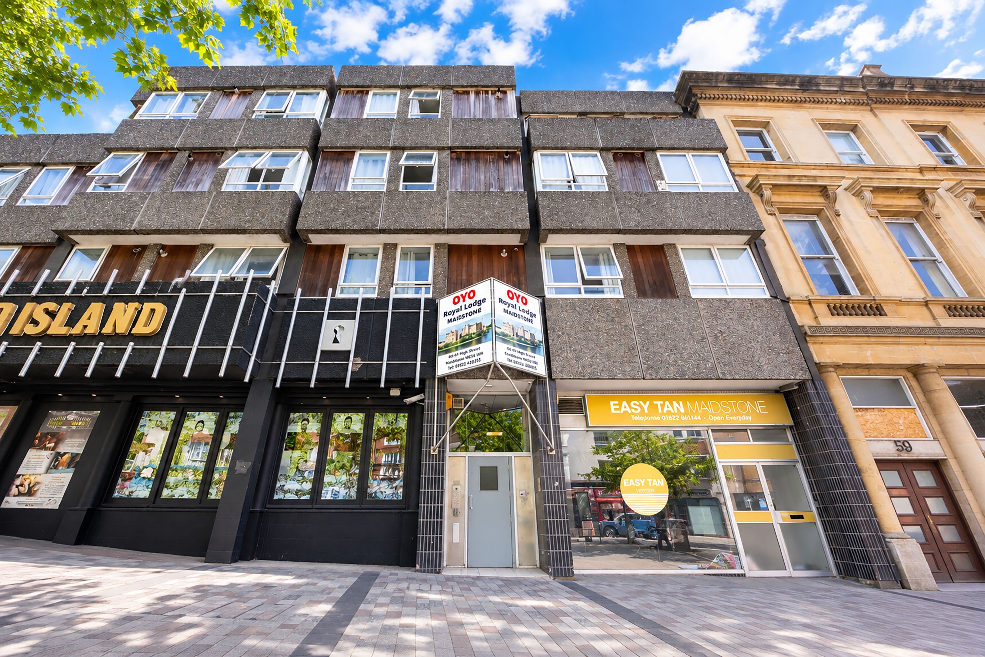 Un edificio de varios pisos con una fachada que dice 'OYO Royal Lodge' y un letrero que indica 'EASY TAN MAIDSTONE' al otro lado de la calle.