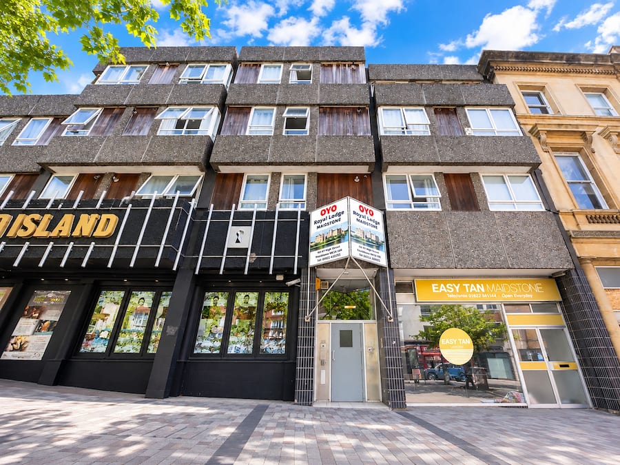 Un edificio de varios pisos con una fachada que dice 'OYO Royal Lodge' y un letrero que indica 'EASY TAN MAIDSTONE' al otro lado de la calle.