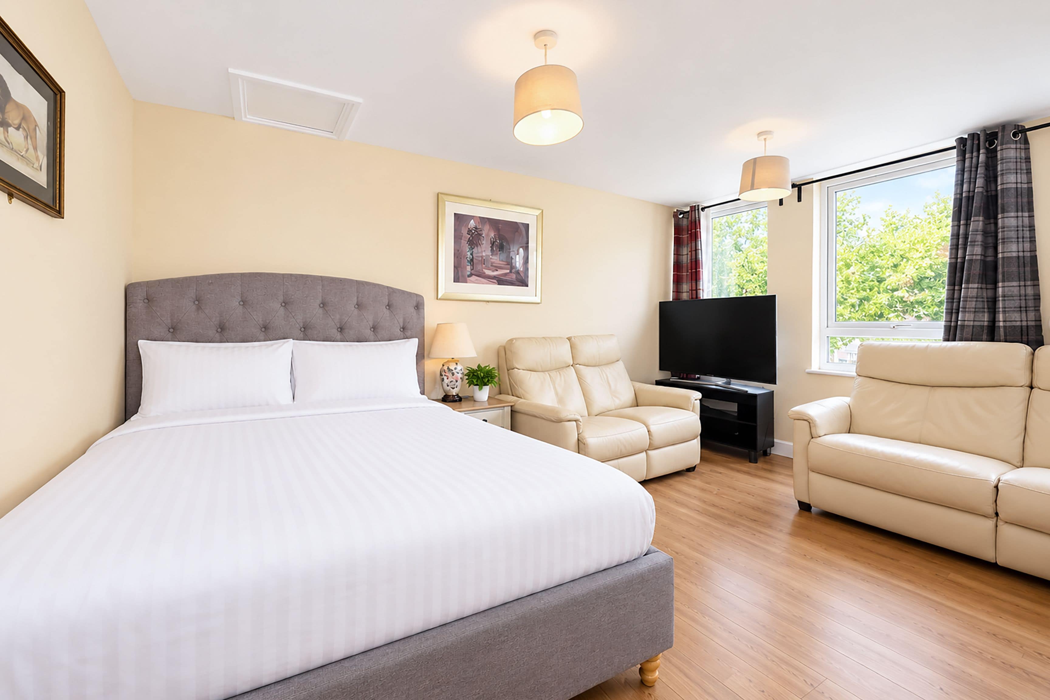 A hotel room with a large bed, two armchairs, a TV, and a window with curtains.