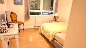 Een slaapkamer met een bed, een bureau, een stoel, een raam en een plafondlamp.