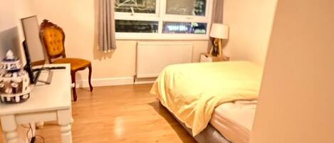 A bedroom with a bed, a desk, a chair, a window, and a ceiling light.