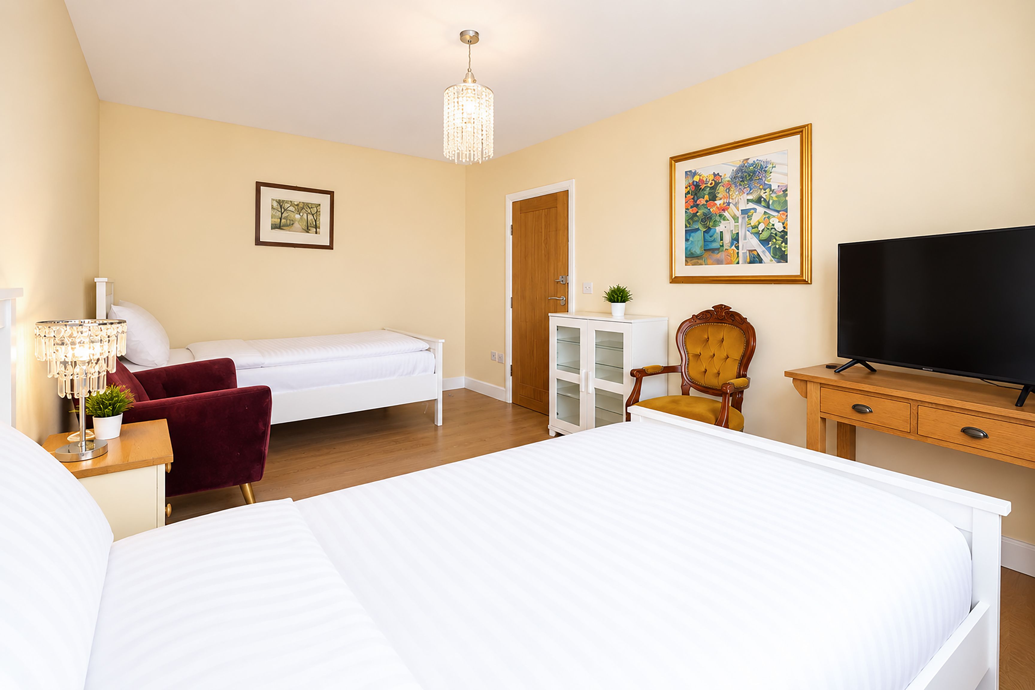 Habitación de hotel con cama, televisión, escritorio, silla, armario y un cuadro en la pared.
