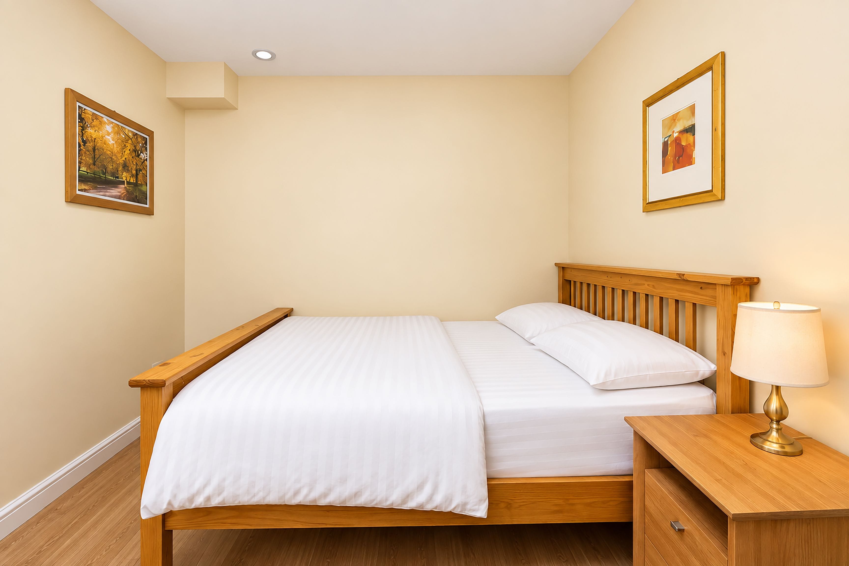 A neatly made bed with white linens, a wooden headboard, and a bedside table with a lamp.
